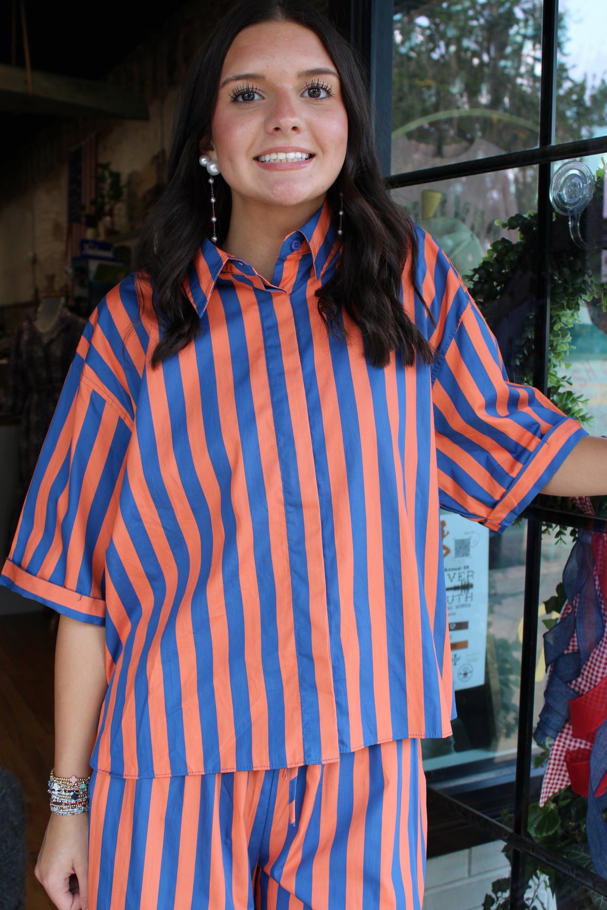 A woman wearing a matching orange and blue vertically striped short-sleeve button-up shirt and striped pants