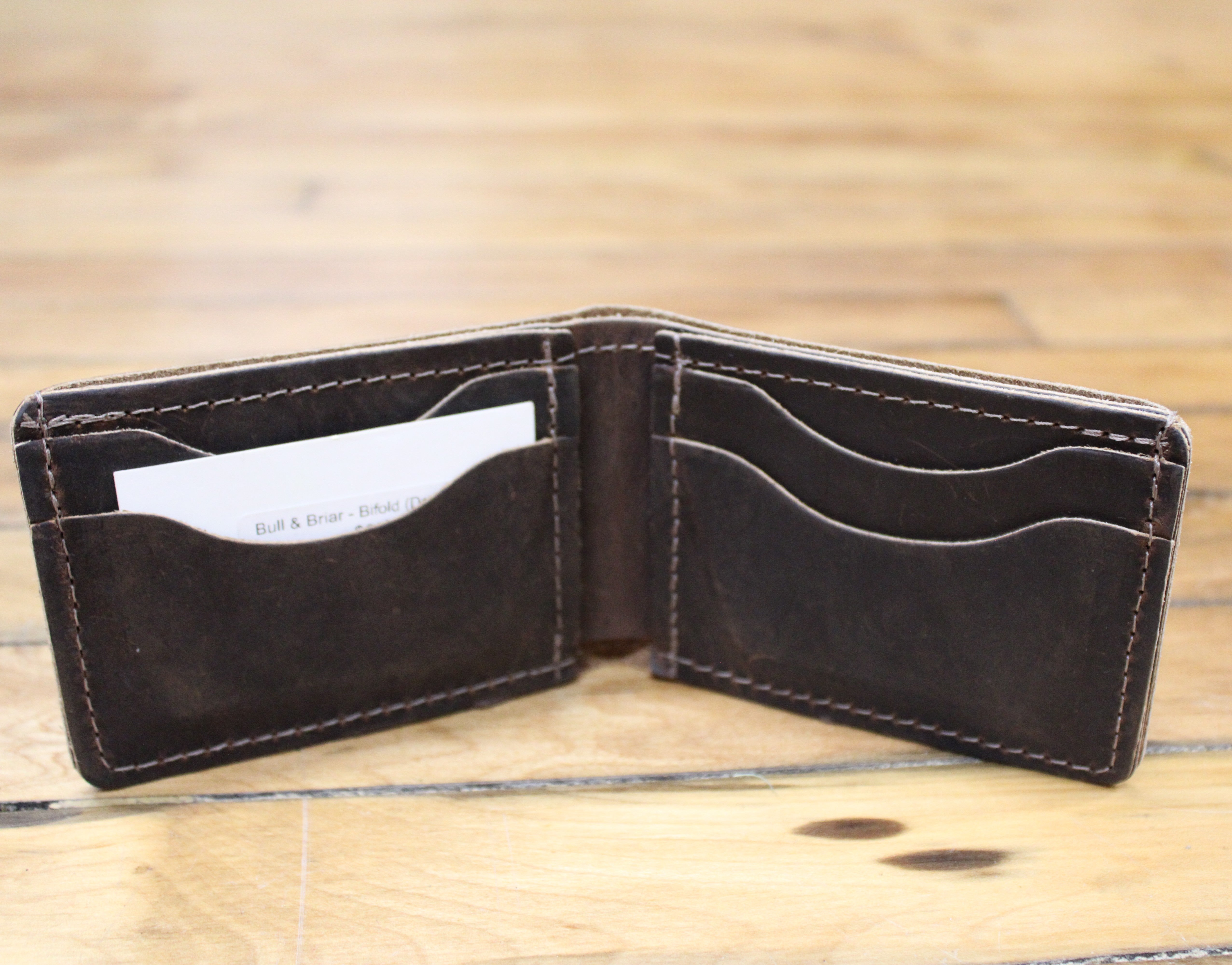 A dark brown leather bifold wallet shown open, displaying its interior card slots and contrast stitching