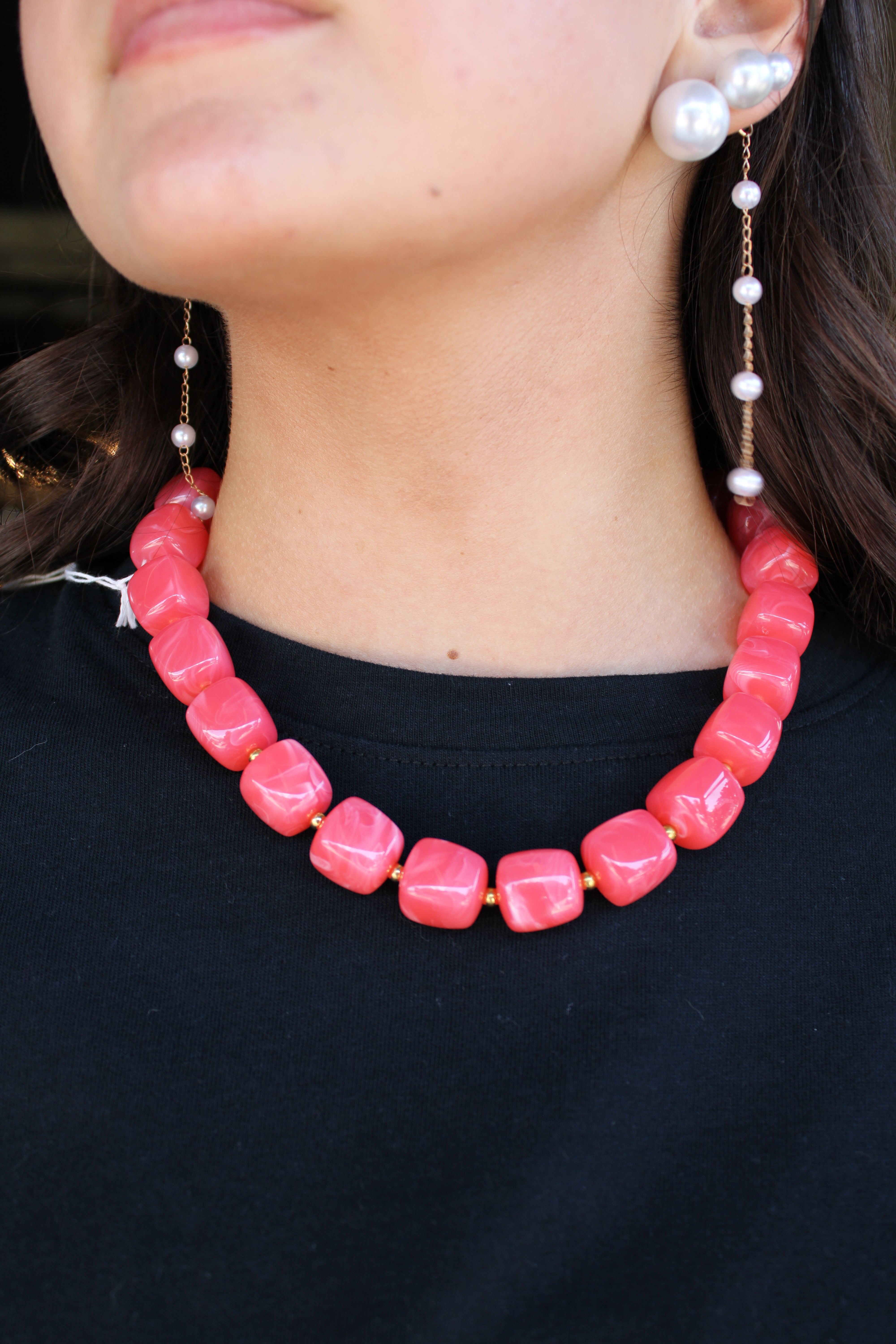 A close-up of a model wearing a chunky coral pink beaded necklace