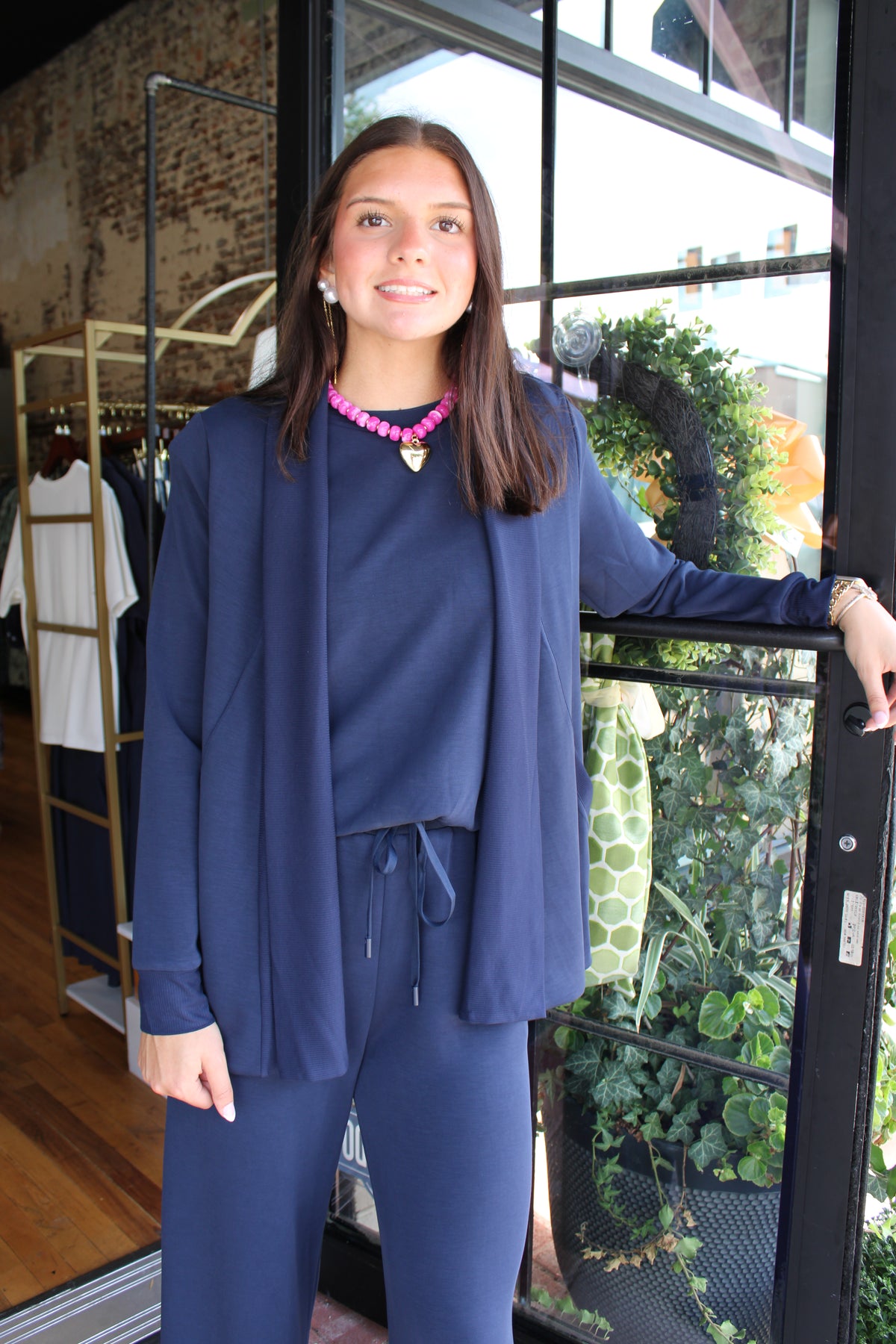 A woman wearing a matching navy blue lounge set consisting of a long-sleeve top and pants with a drawstring waist, standing in a shop next to a window.
