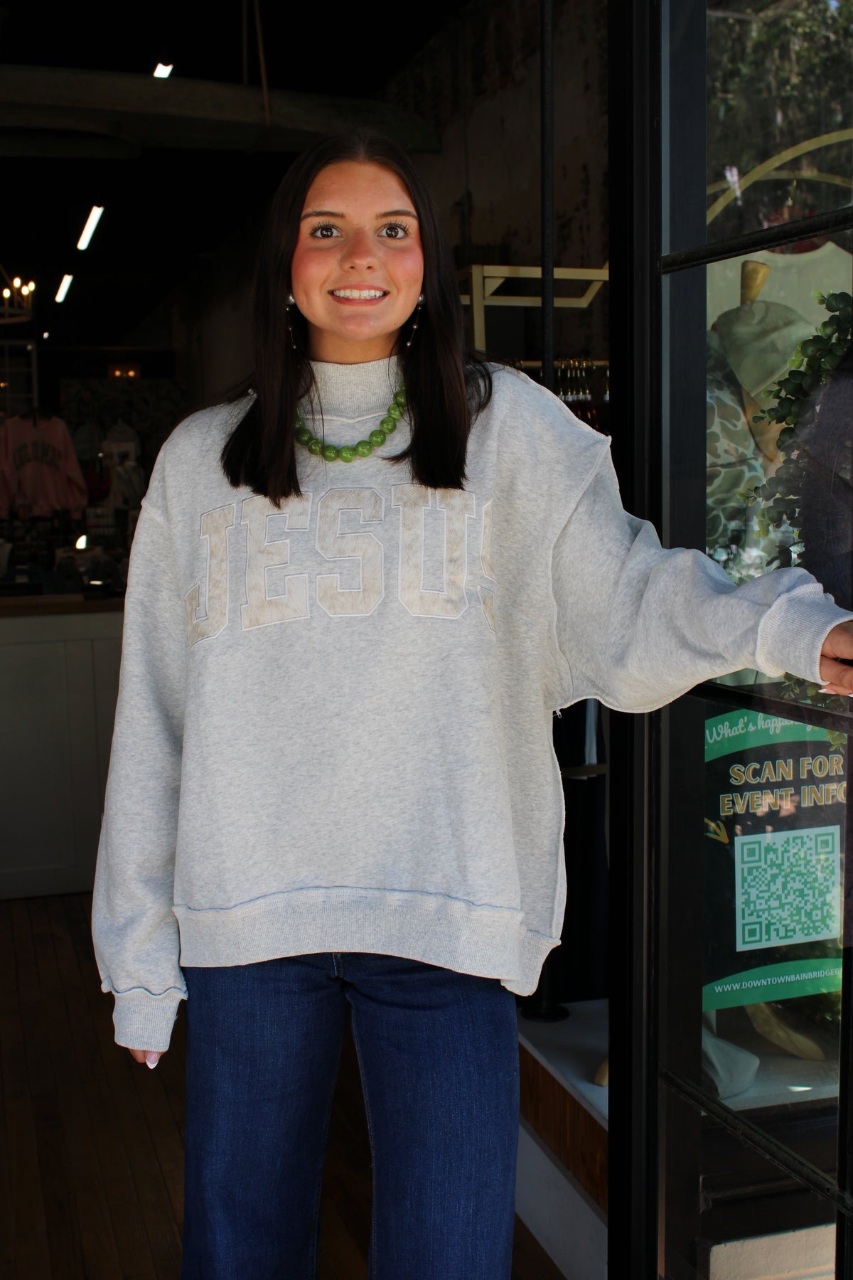 woman wearing gray mock neck sweater with "Jesus" spelled out on embroidered fabric on the front