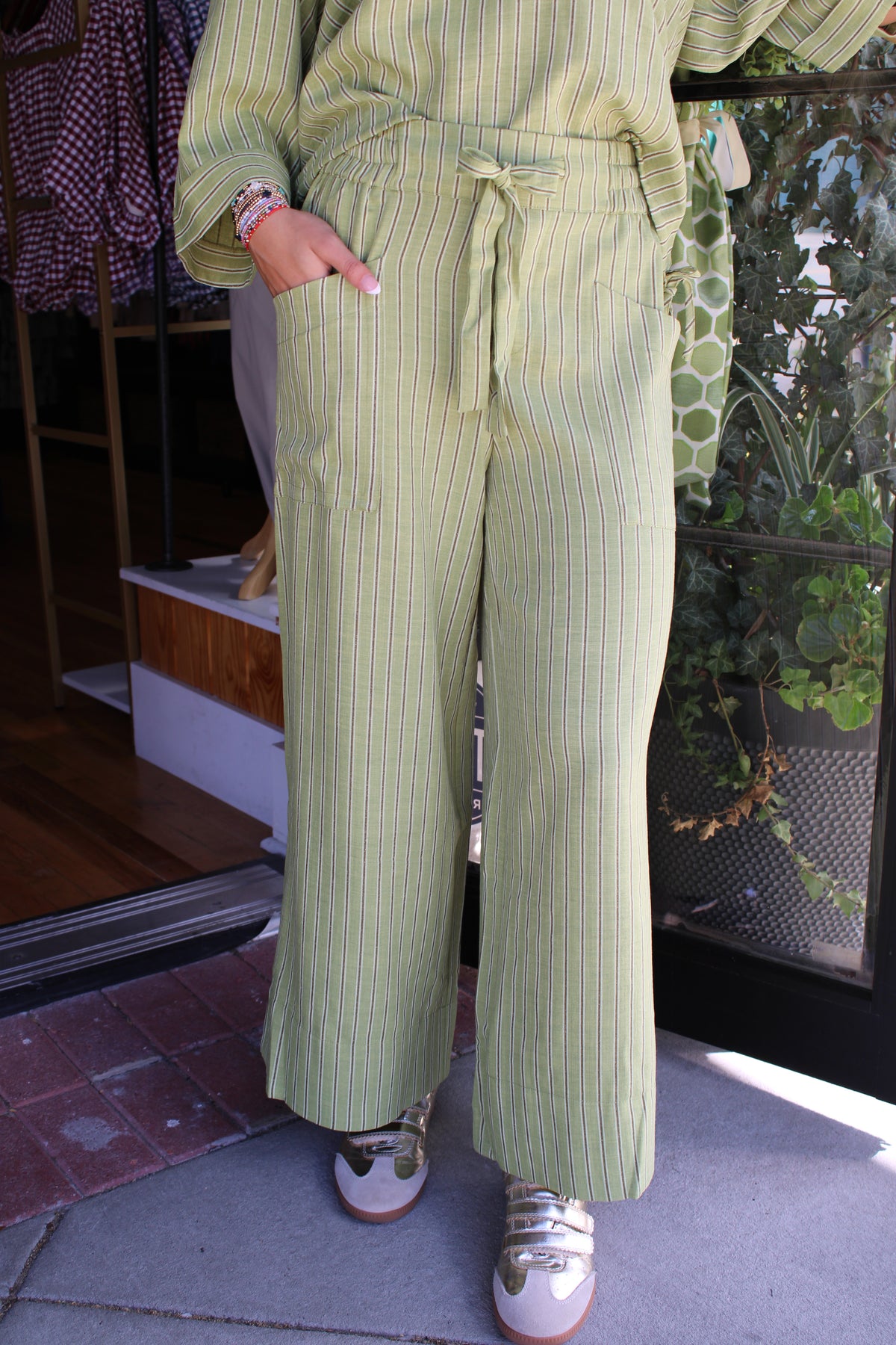 A person wearing light olive green wide-leg pants with thin vertical darker green stripes, paired with a matching top and white sneakers, standing on a sidewalk.