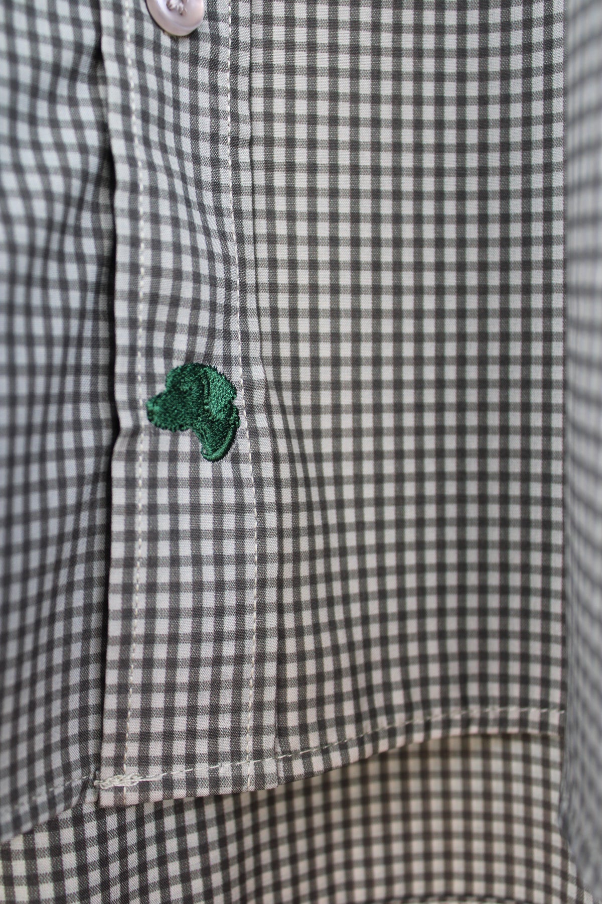 Close-up of a mens button up shirt with a small green embroidered clover detail on the flap.