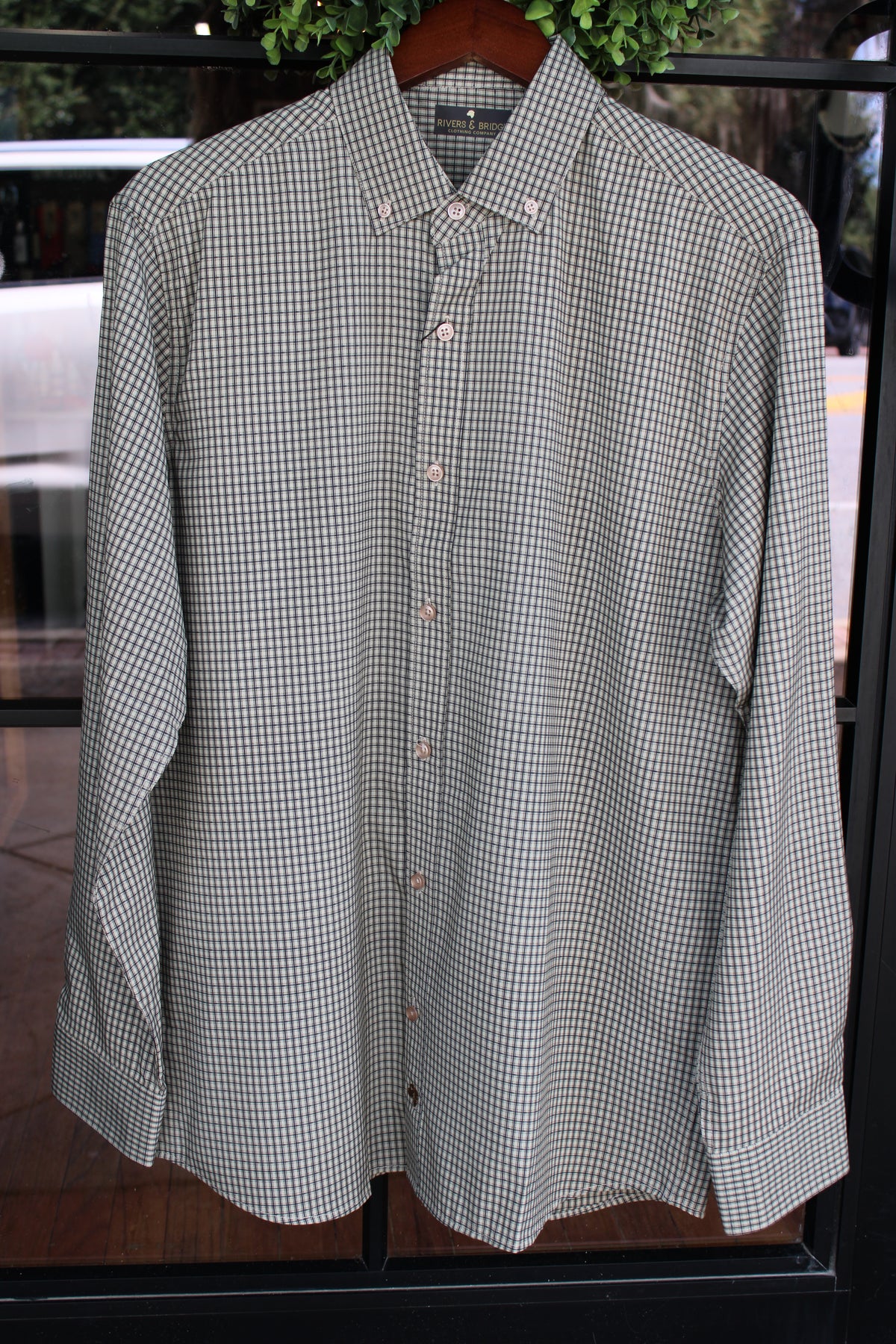 A long-sleeve button-down shirt with a small-scale green and white gingham check pattern, hanging on a wooden hanger.