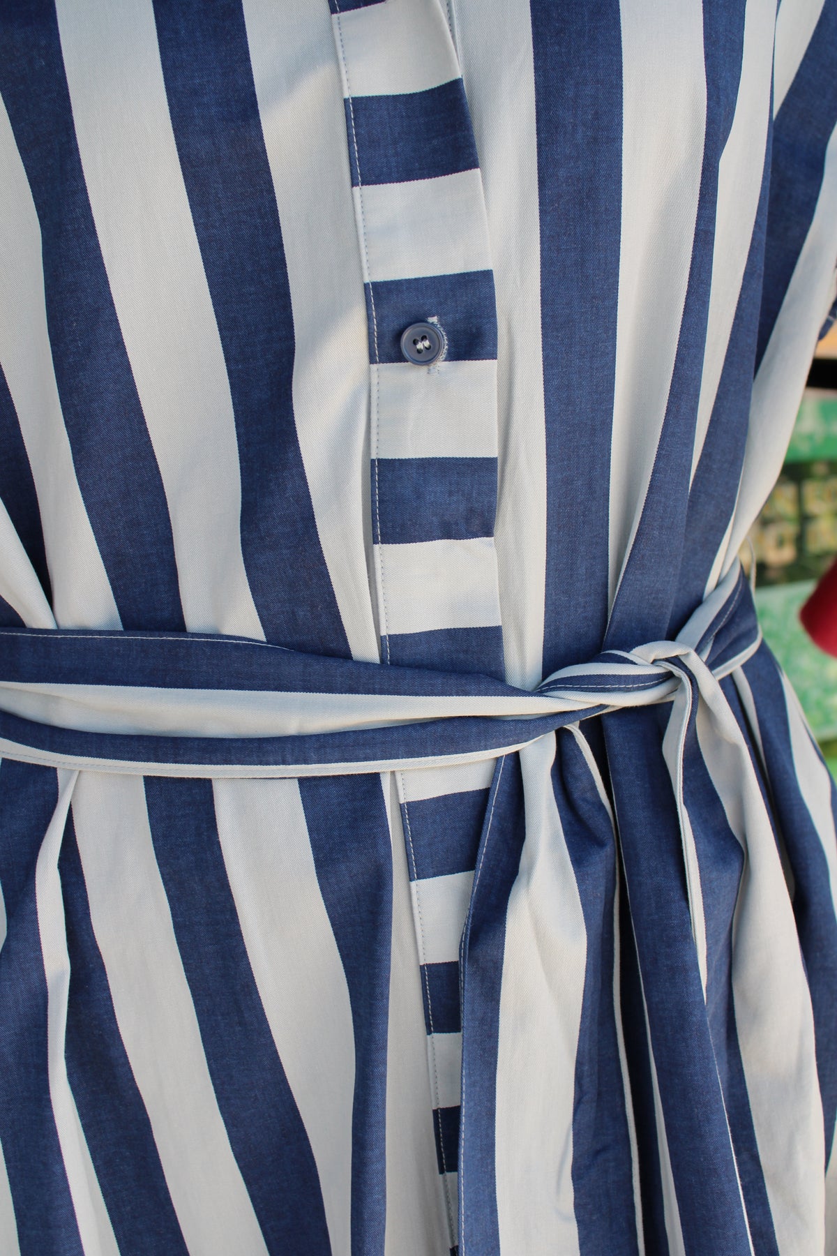 Close-up of a blue and white vertically striped dress with a matching tie belt and a buttoned front placket.