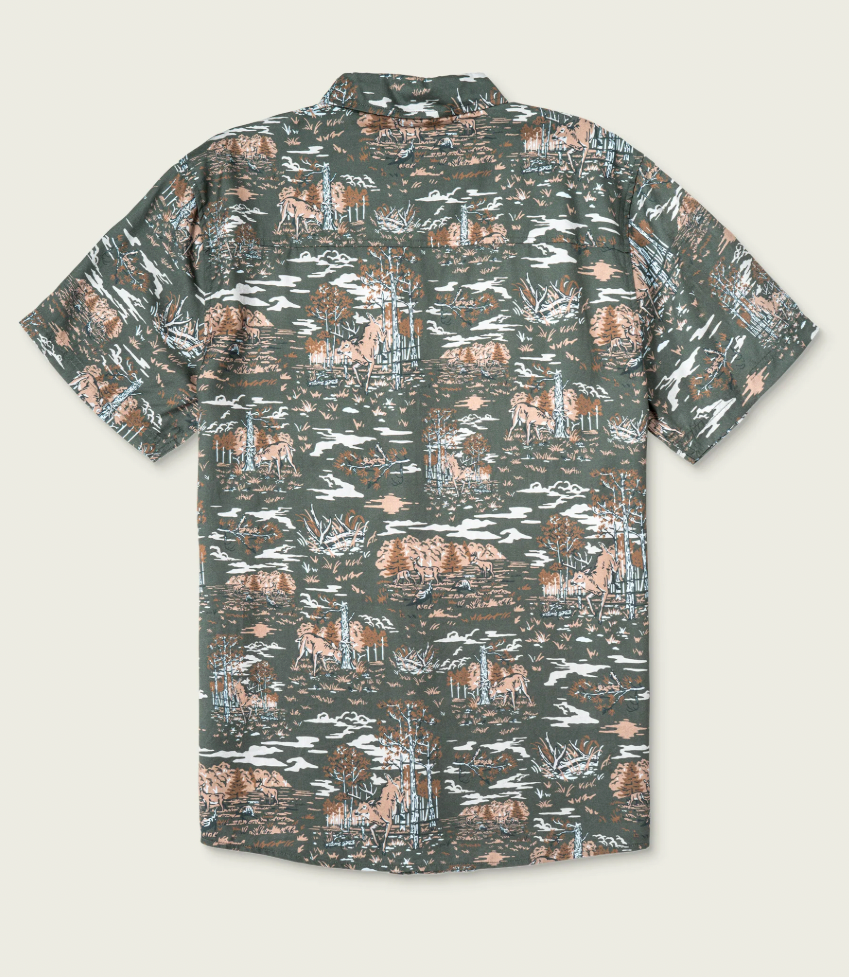 A short-sleeve button-up shirt with an all-over camouflage-style print featuring brown deer, white trees, and blue-gray brush on a muted olive green background, shown flat against a light beige backdrop.