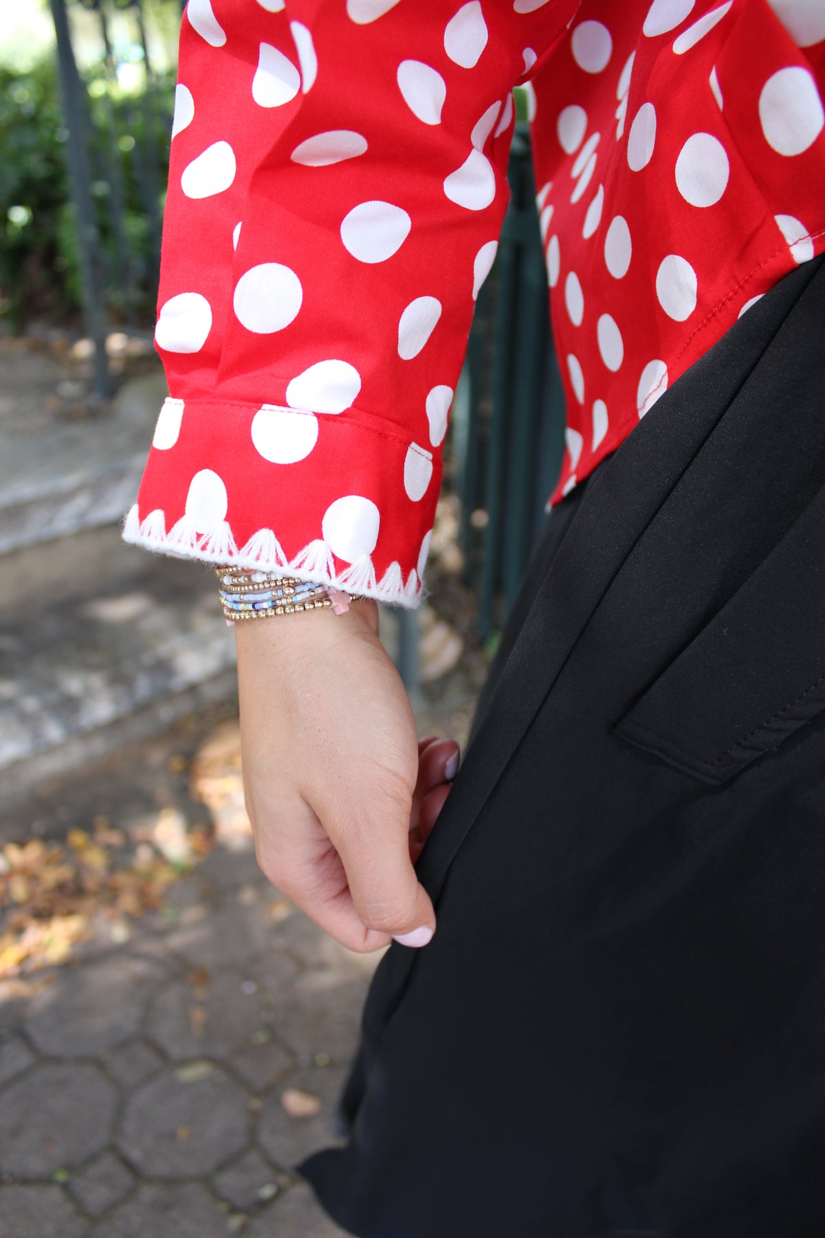 A close-up lifestyle shot of a person wearing a red long-sleeve top with white polka dots and a black skirt, standing outdoors.