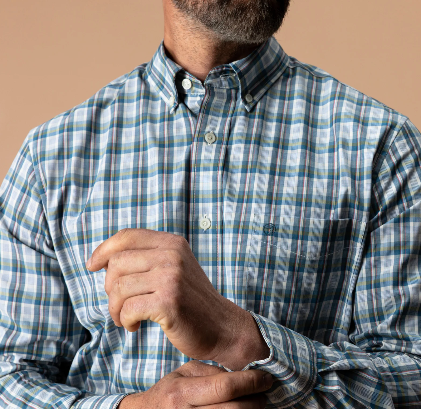 A close-up of a man wearing a long-sleeve button-down shirt with a blue, yellow, and red plaid pattern, against a solid beige background.