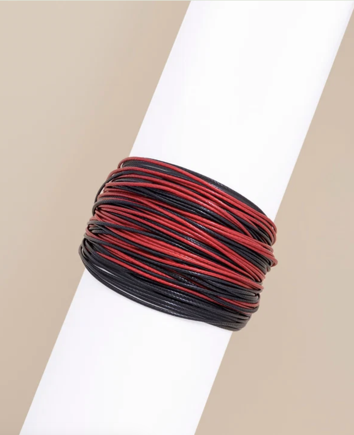 A multi-layer wrap bracelet with alternating red and black cords, displayed on a white cylindrical mannequin arm against a neutral beige background.
