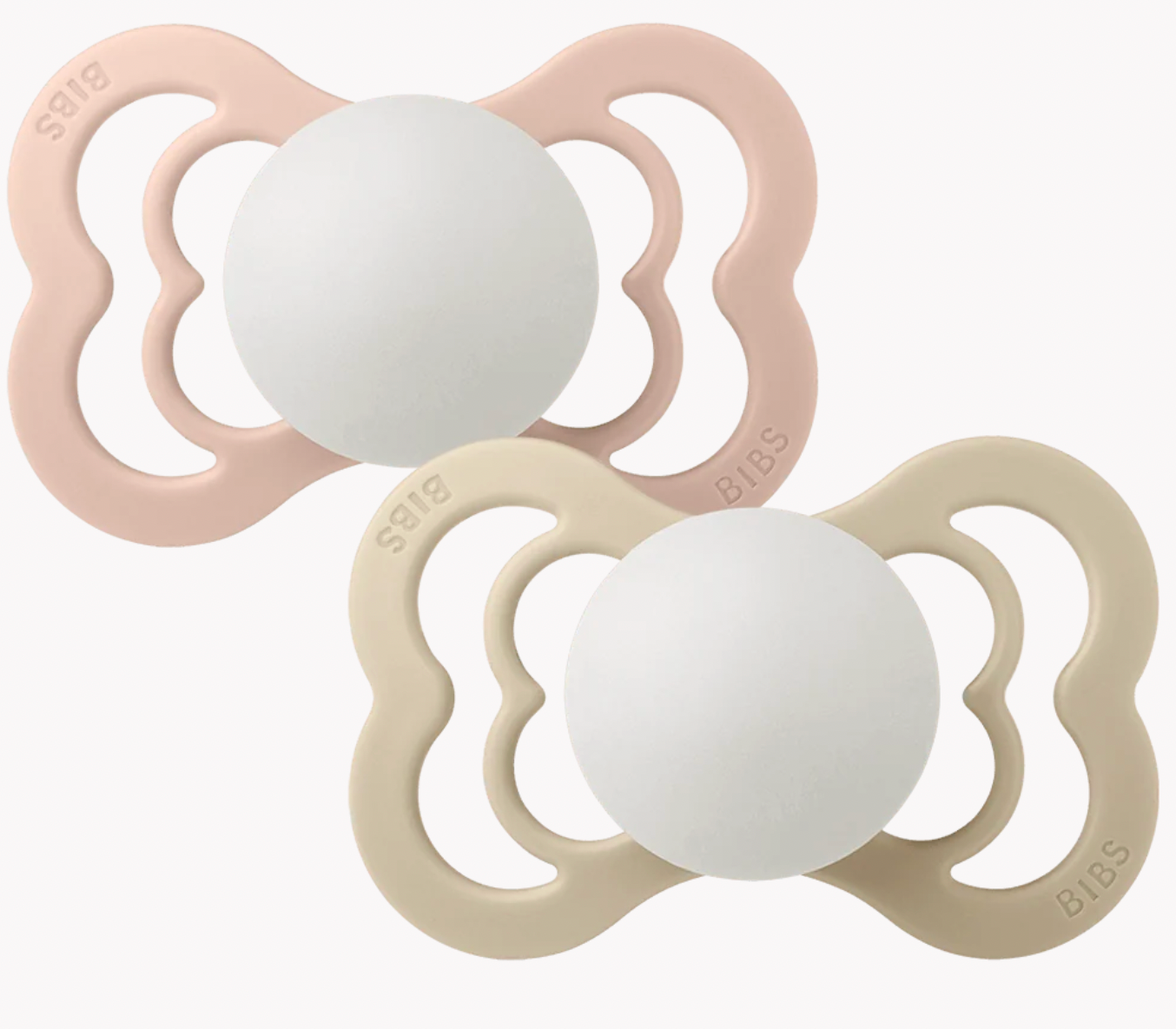 Two BIBS pacifiers with white silicone centers and one in dusty pink and one in light beige, arranged diagonally on a clean white background. Glow in the dark