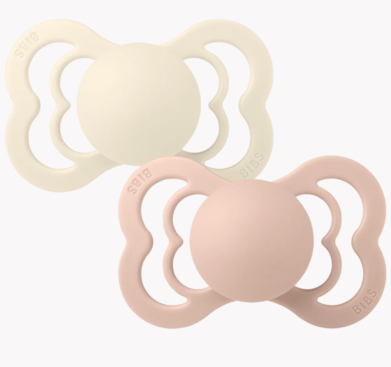 Two silicone baby pacifiers on a clean white background, one in cream and one in pale pink, both with the brand name 'BIBS' embossed on the sides.
