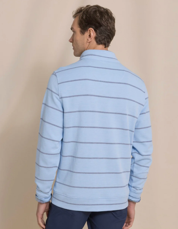 A man viewed from the back wearing a light blue long-sleeve quarter-zip pullover with thin dark horizontal stripes, paired with navy trousers, against a solid beige background.