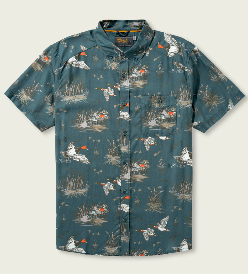 A short-sleeve button-up shirt in a muted teal-blue color, featuring an all-over print of mallards and reeds in white, orange, and brown. The shirt has a pointed collar, button-down front, and a chest pocket.