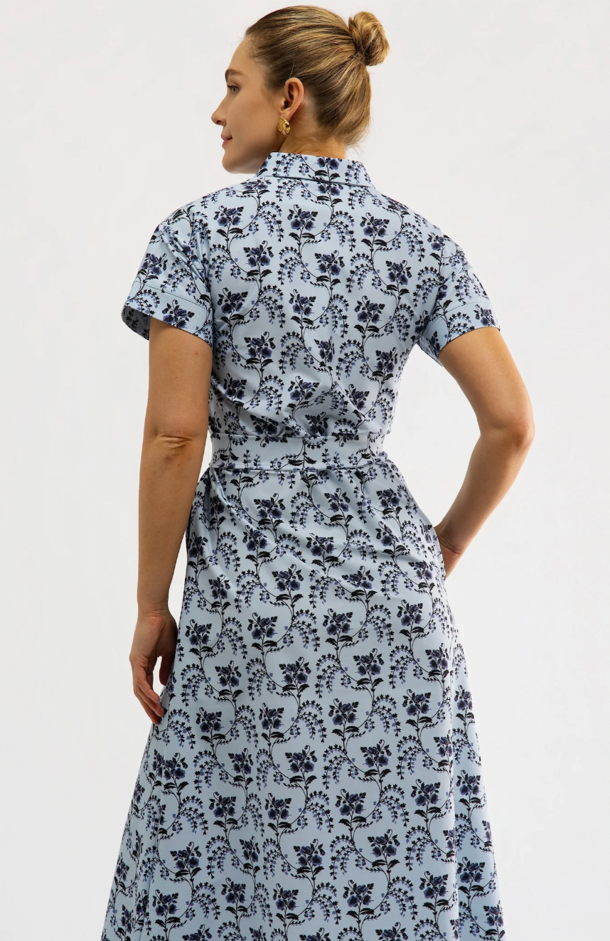 A woman shown from the back wearing a light blue short-sleeve midi dress with a dark navy floral block print and a matching waist tie, set against a plain white studio background.