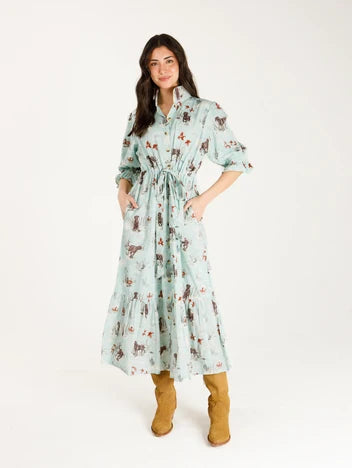 Woman wearing long blue dress that cinches at the waist and includes prints of dogs and ducks