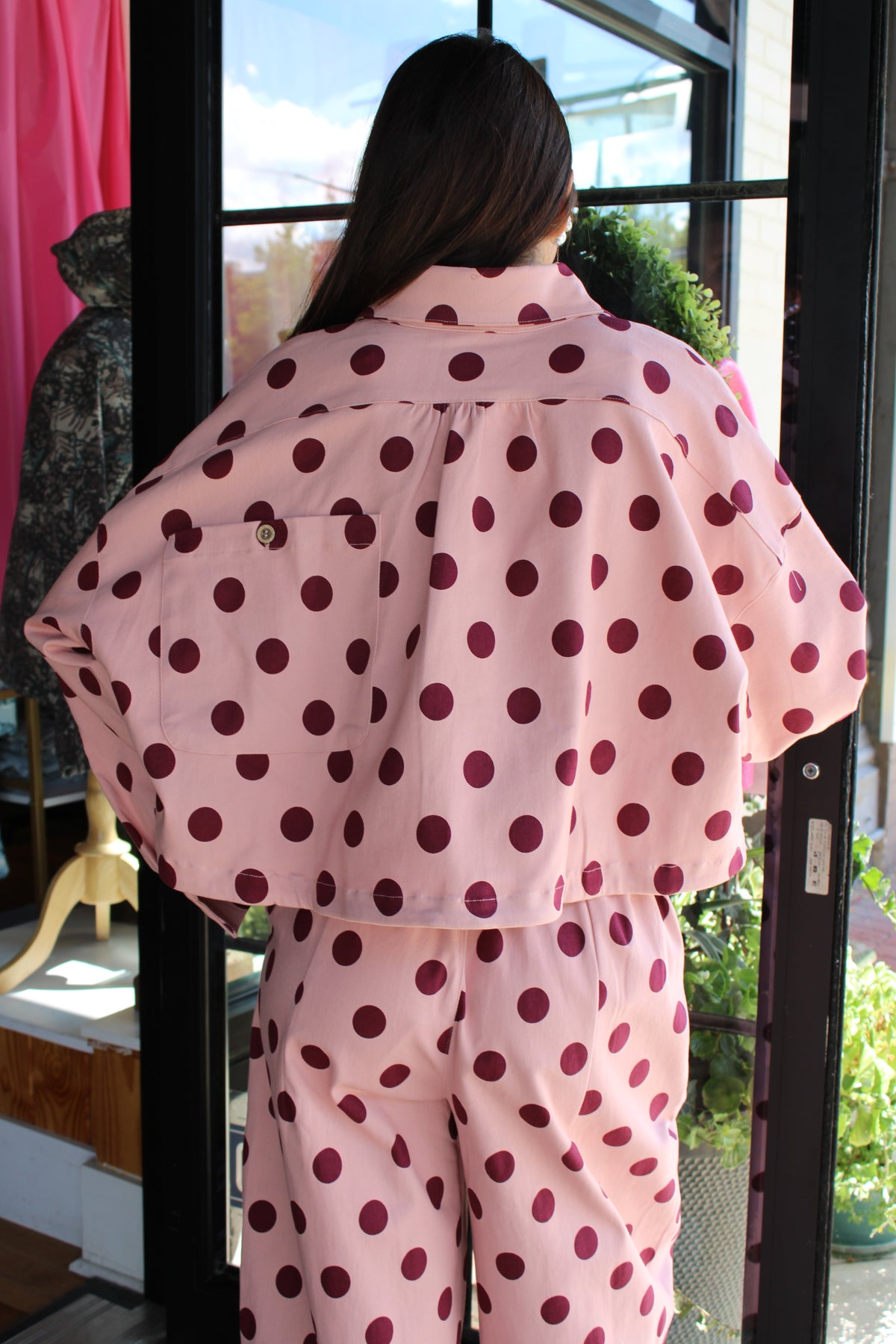 A person viewed from behind wearing a light pink jacket with dark burgundy polka dots, standing in front of a glass door.