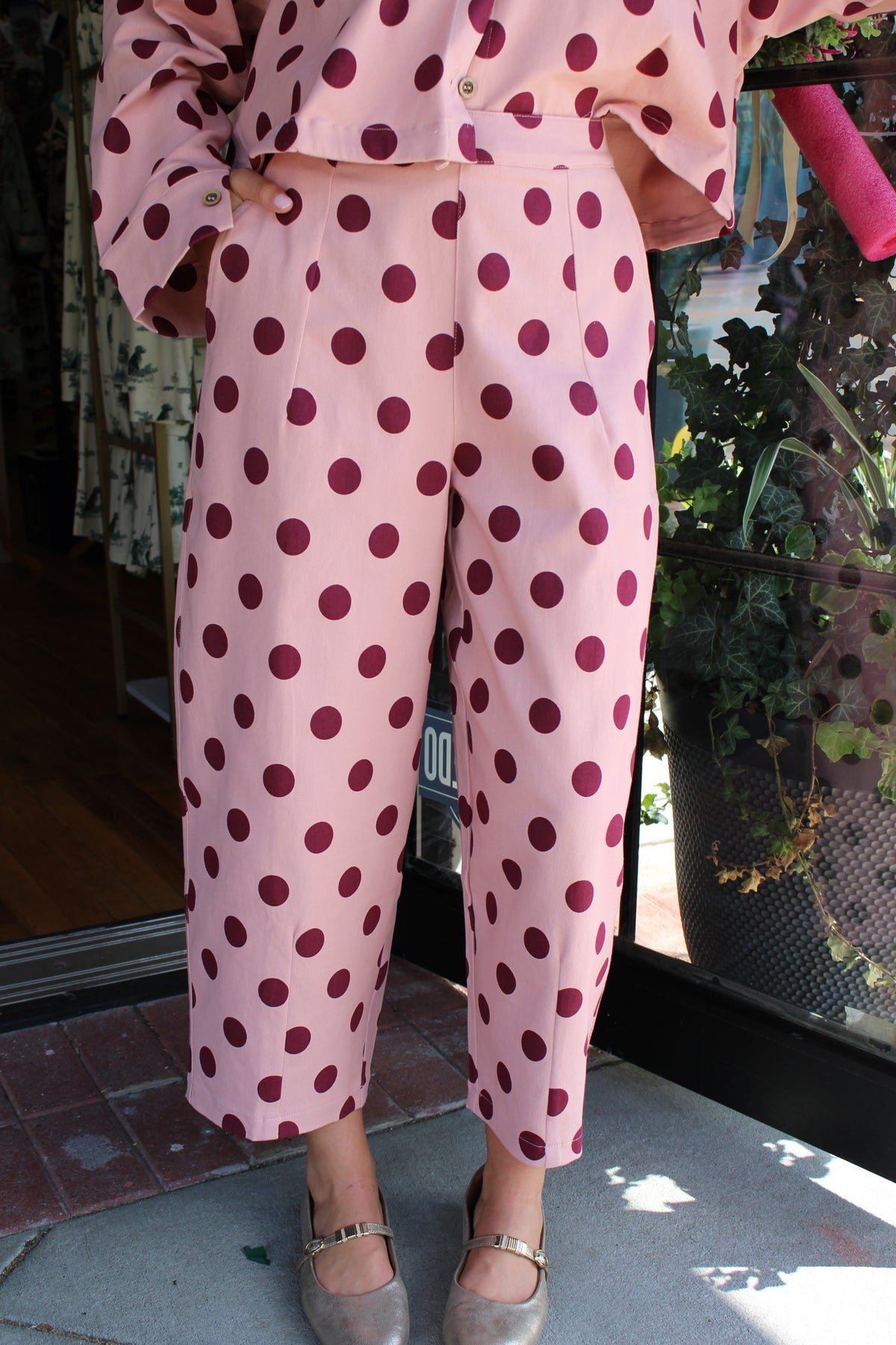A person wearing a light pink two-piece outfit with dark burgundy polka dots, featuring cropped pants, paired with metallic silver shoes.