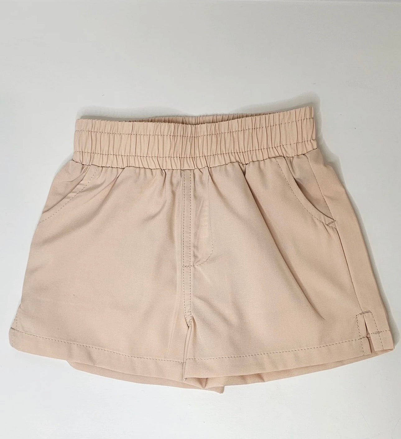A pair of beige elastic-waist shorts with side pockets, laid flat on a light gray background.