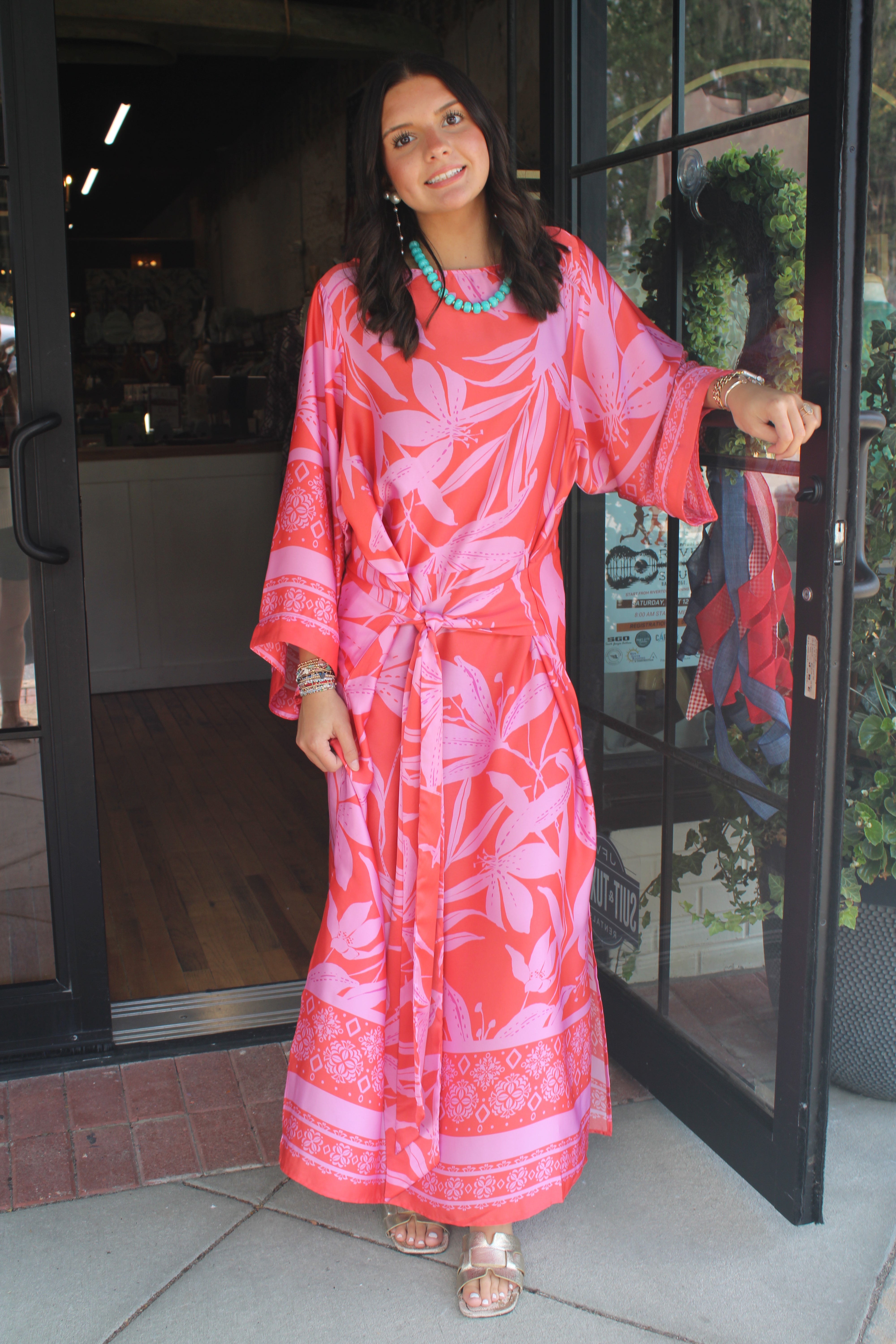 A woman wearing a vibrant pink and coral tropical print kaftan dress