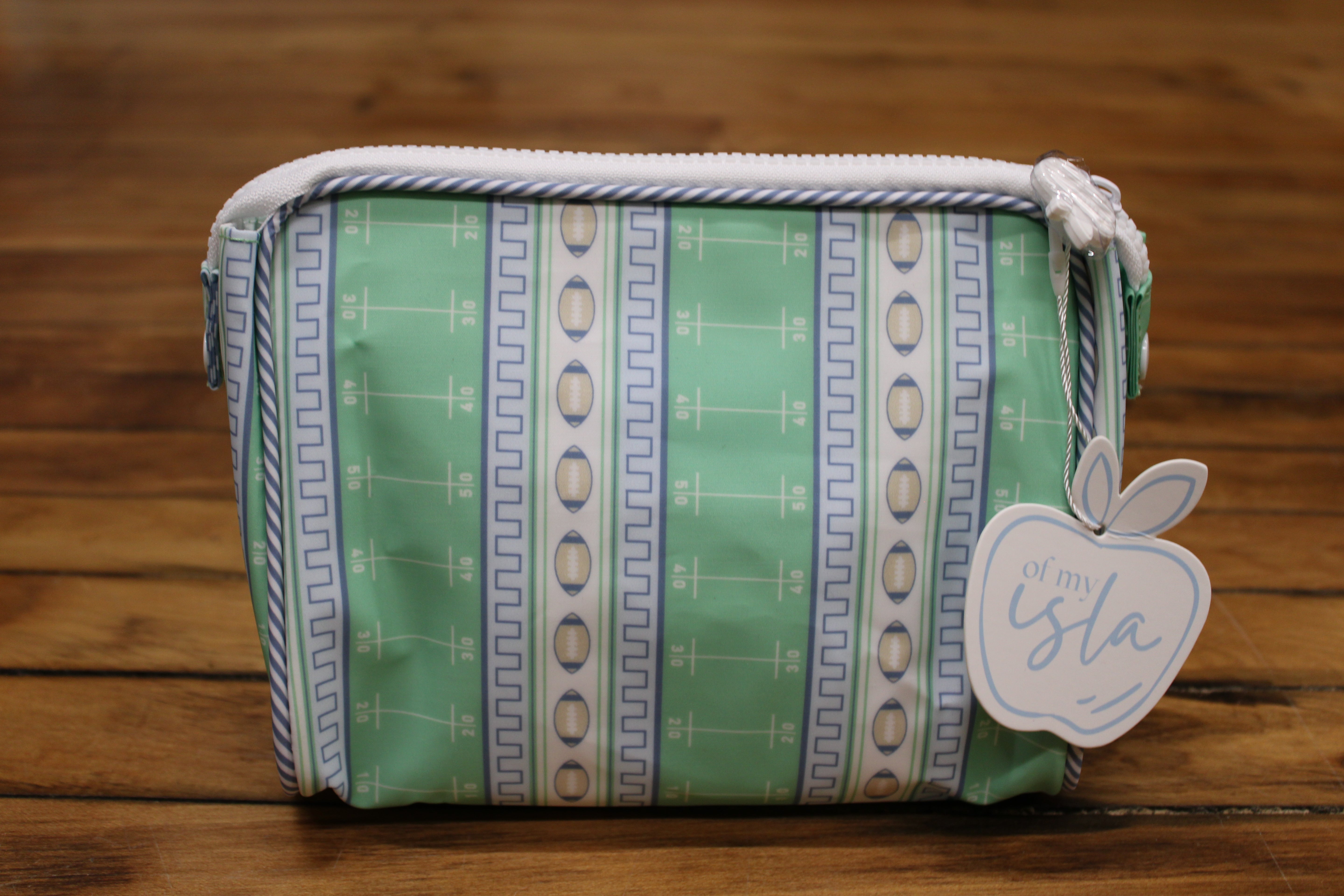 A zippered pouch with a mint green, blue, and white geometric pattern. It features a white zipper, a white hanging tag with an apple cutout that reads 'apple of my isla'
