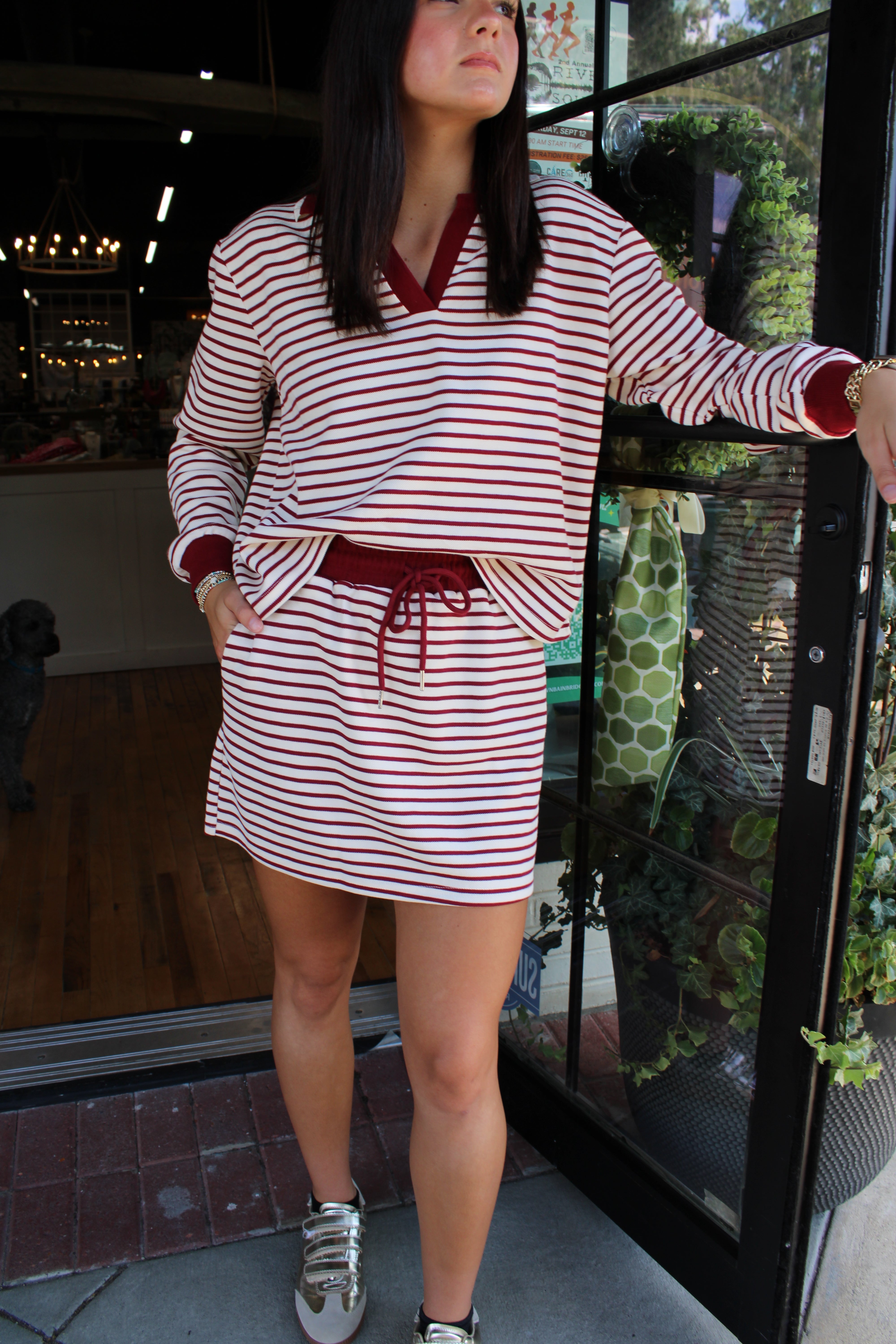 A woman wearing a red and white striped long-sleeve skort set with a V-neck and drawstring waist, standing in front of a glass storefront door.