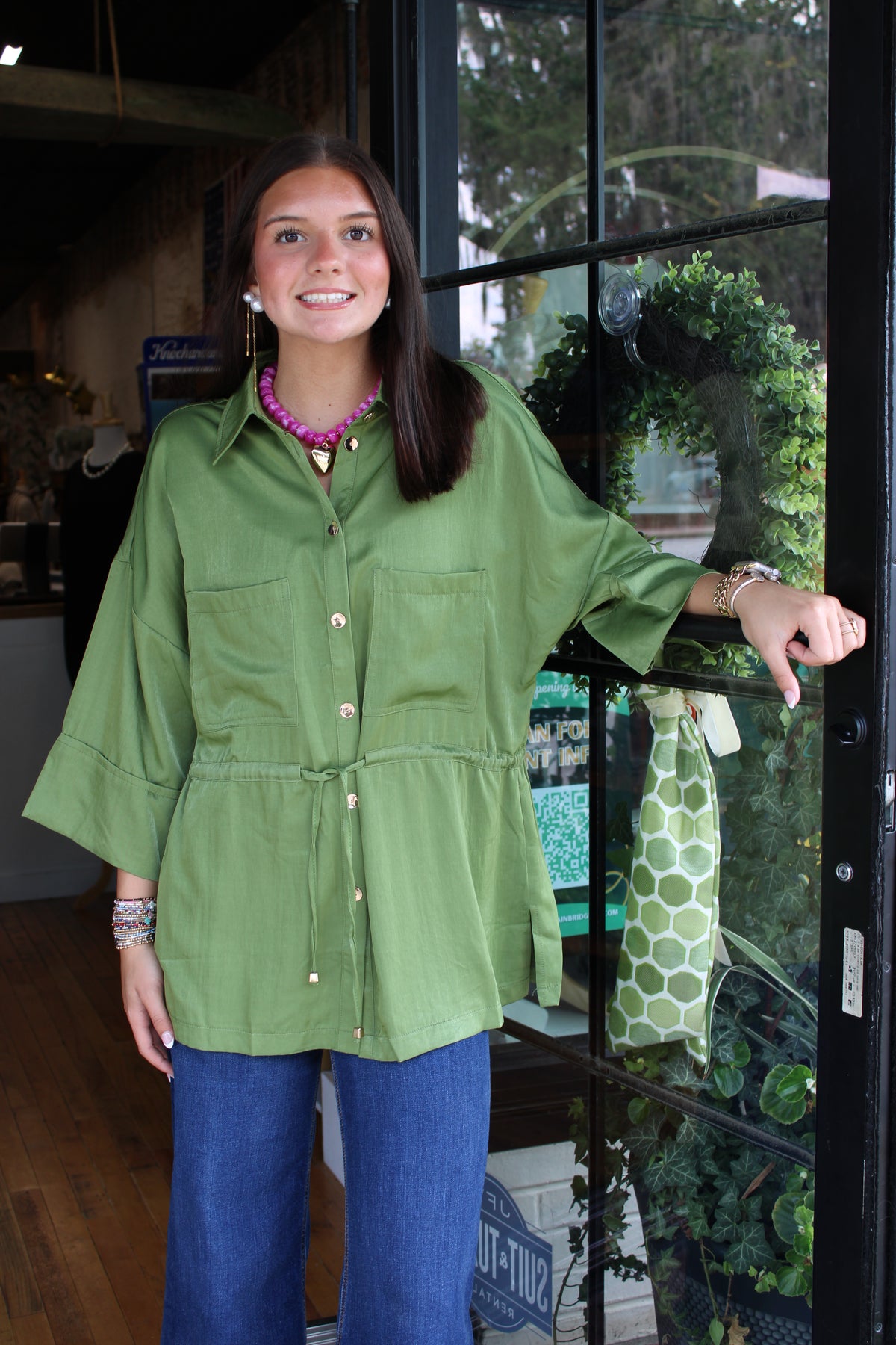 woman wearing a green top with a drawstring at the waist and gold buttons down the front