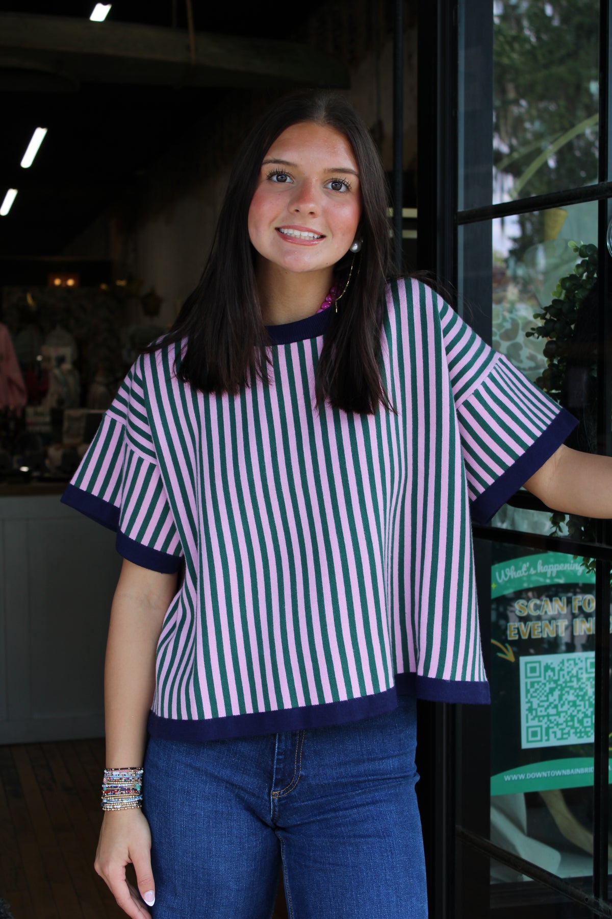 woman wearing a pink and green striped short sleeve, sweater top with navy blue trim