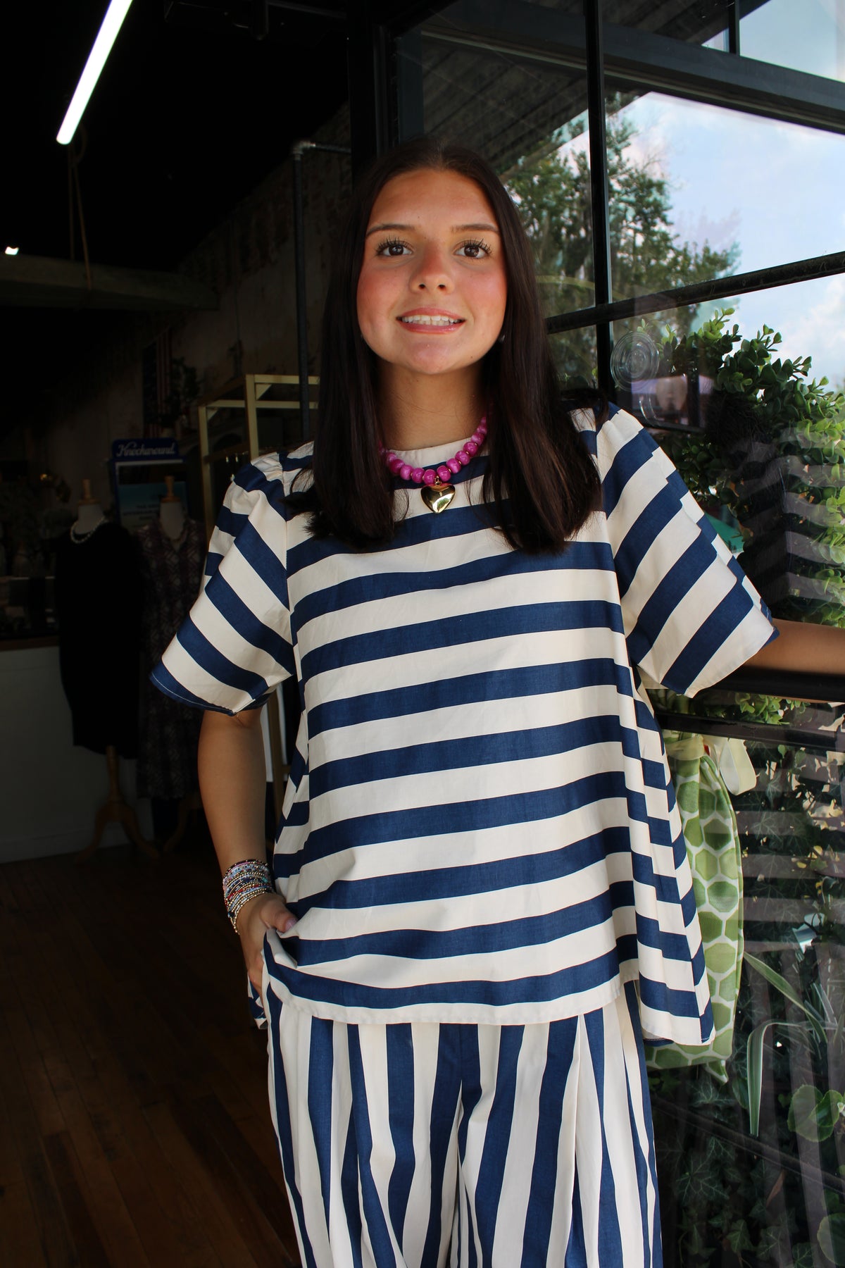 A woman wearing a matching navy blue and white striped tunic top and wide-leg pants set, standing in a shop interior.