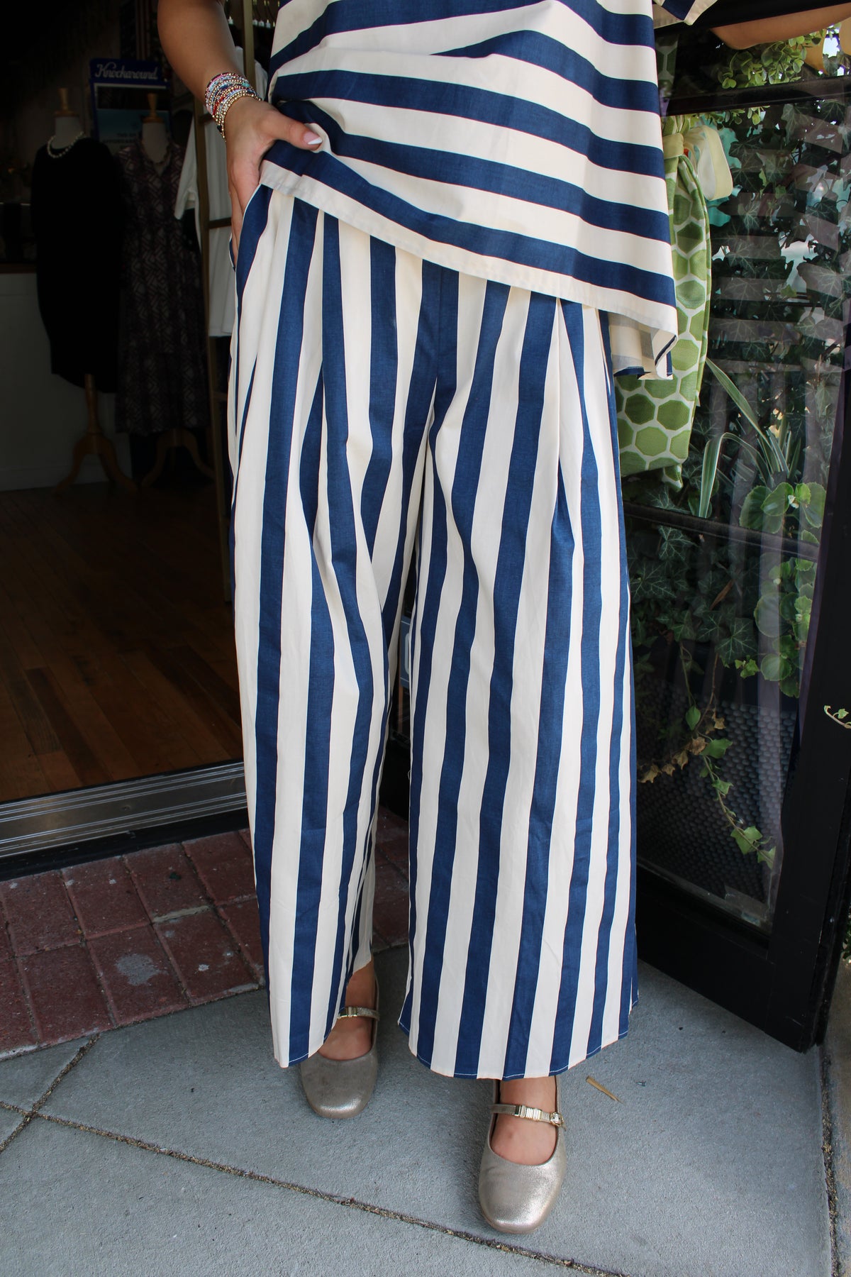 A person wearing navy and white vertically striped wide-leg pants with a matching striped top, standing on a tiled floor in front of a storefront.