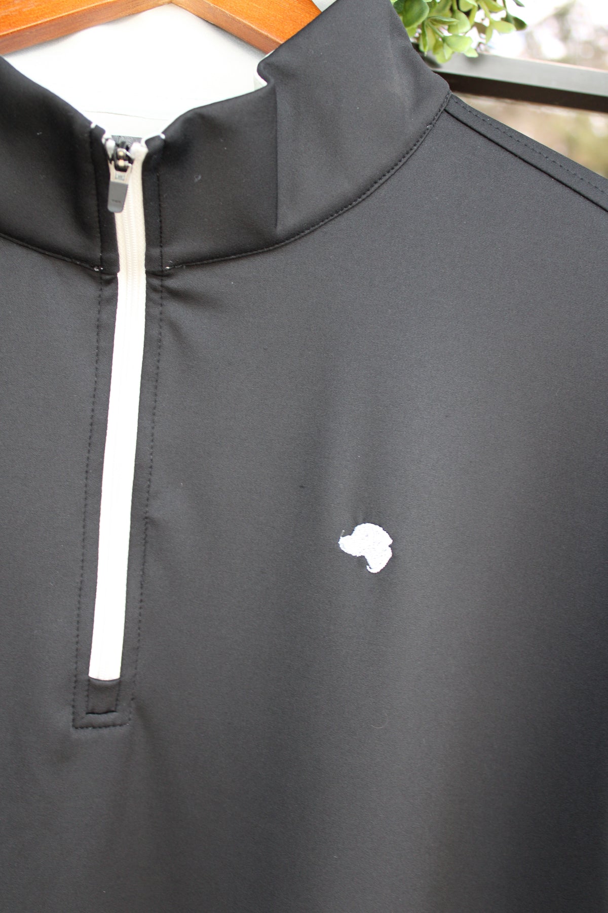 close up of a silver dog logo and zipper on a black quarter zip 