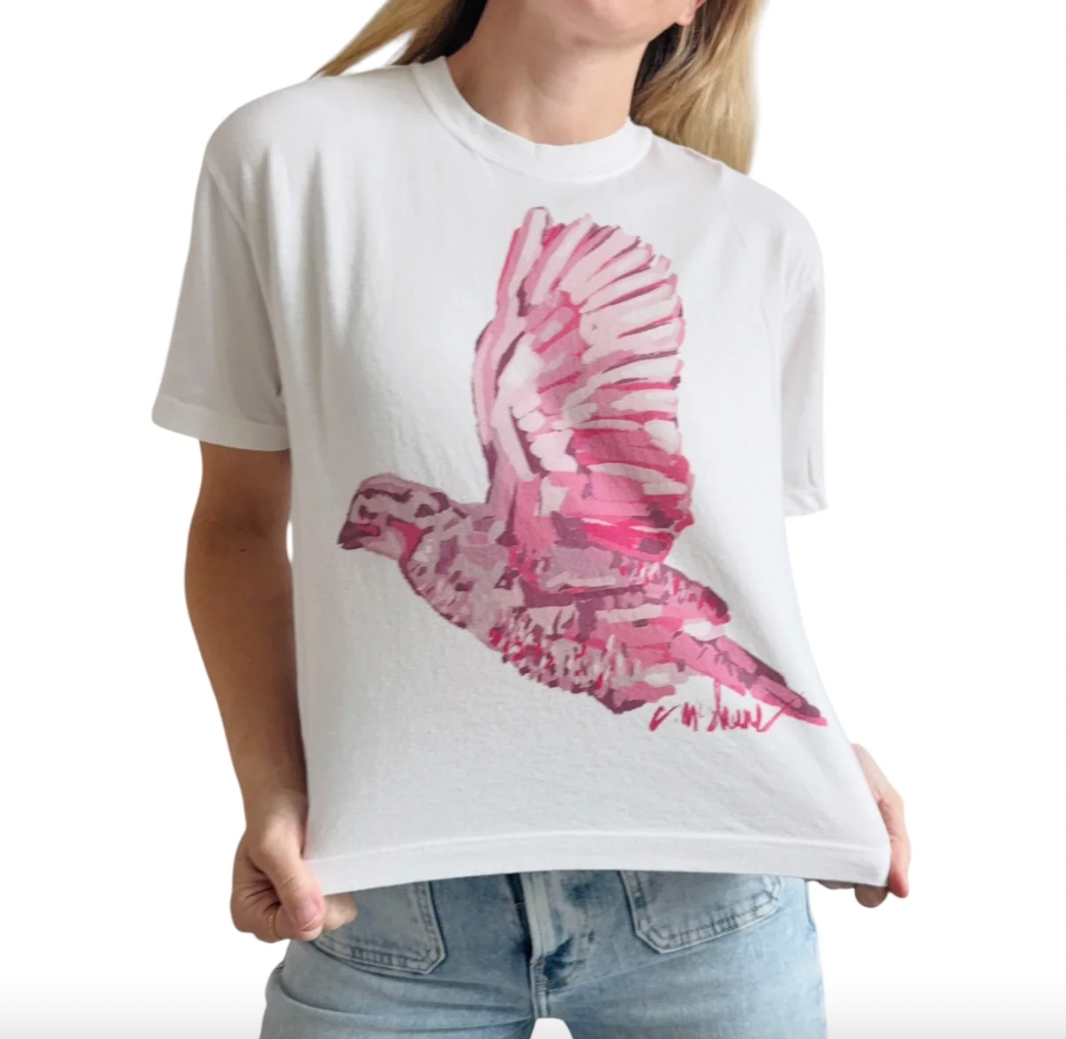 A person wearing a white short-sleeve T-shirt with a large pink acrylic style quail graphic on the front, paired with light blue jeans, against a plain white background.
