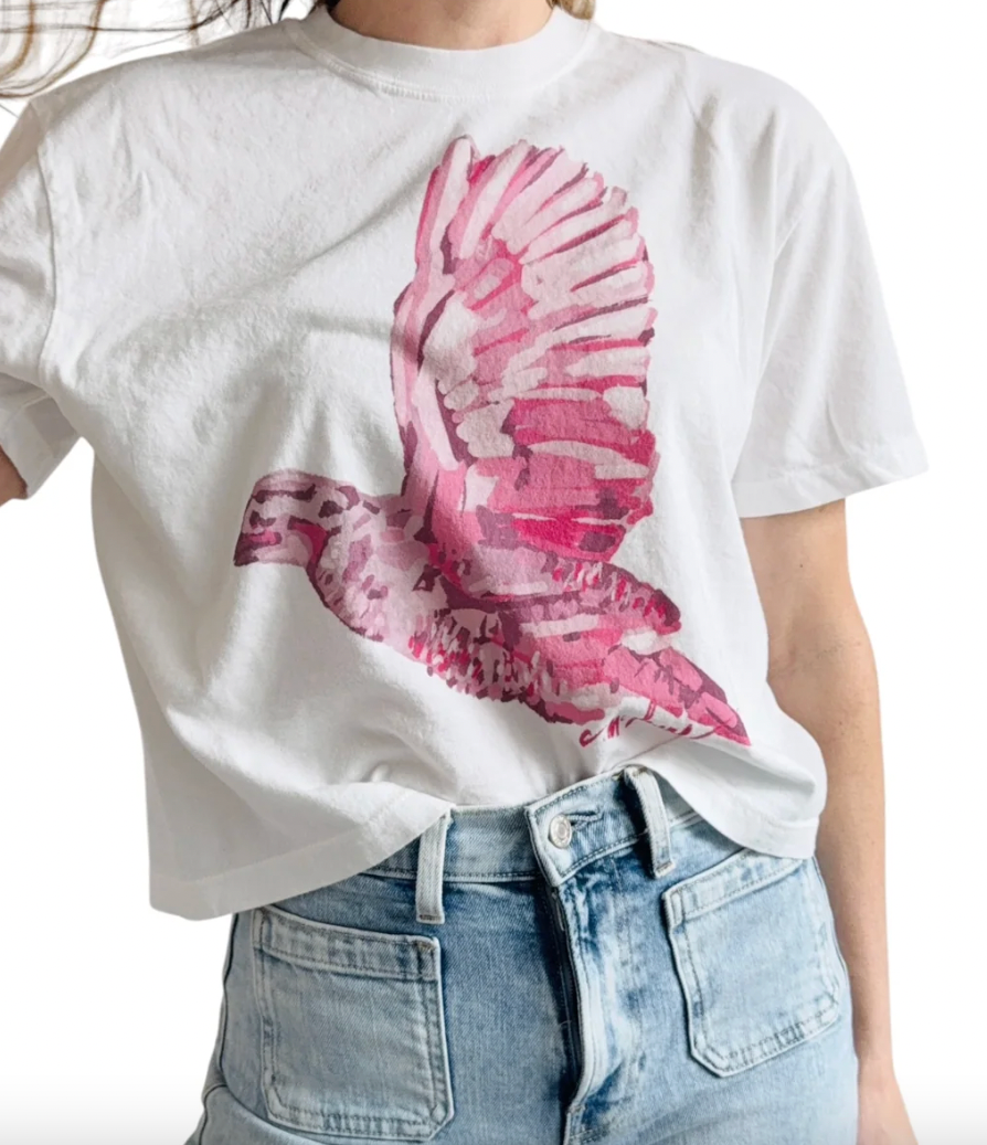 A person wearing a white short-sleeve T-shirt with a large pink acrylic style quail graphic on the front, paired with light blue jeans, against a plain white background.