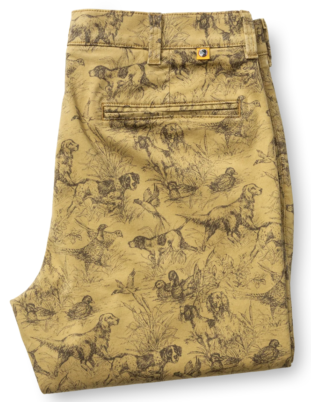 A pair of folded tan chinos featuring an all-over black sketch print of hunting dogs, hounds, and birds. The pants include a button waistband, belt loops, and a rear welt pocket.
