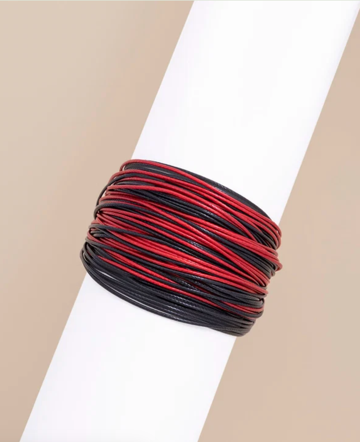 A multi-layer wrap bracelet with alternating red and black cords, displayed on a white cylindrical mannequin arm against a neutral beige background.
