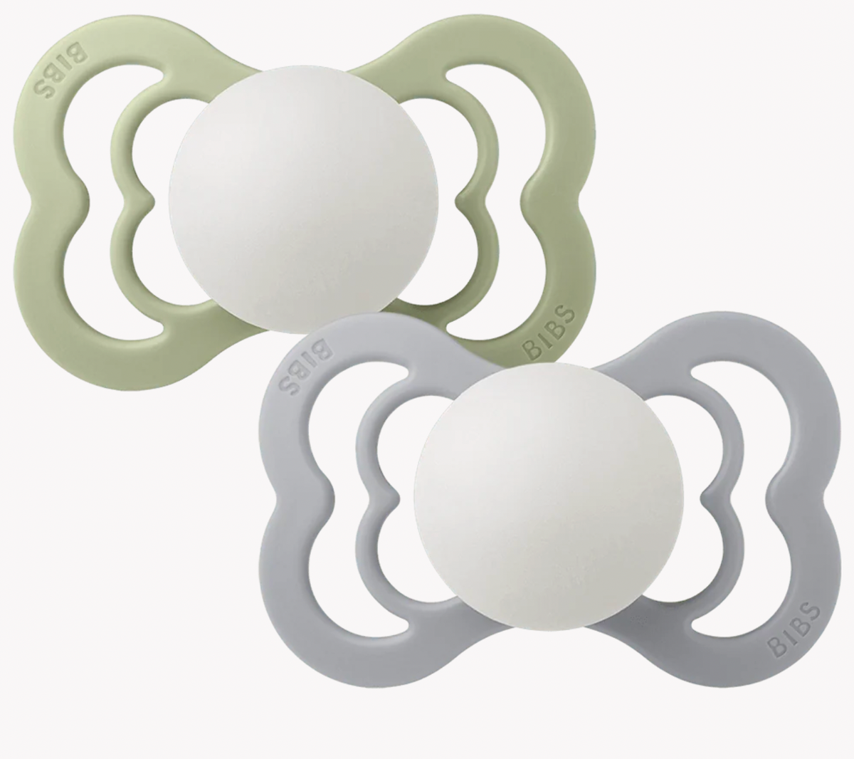 Two BIBS pacifiers on a clean white background, one in sage green and one in light gray, both with white centers. Glow in the dark.