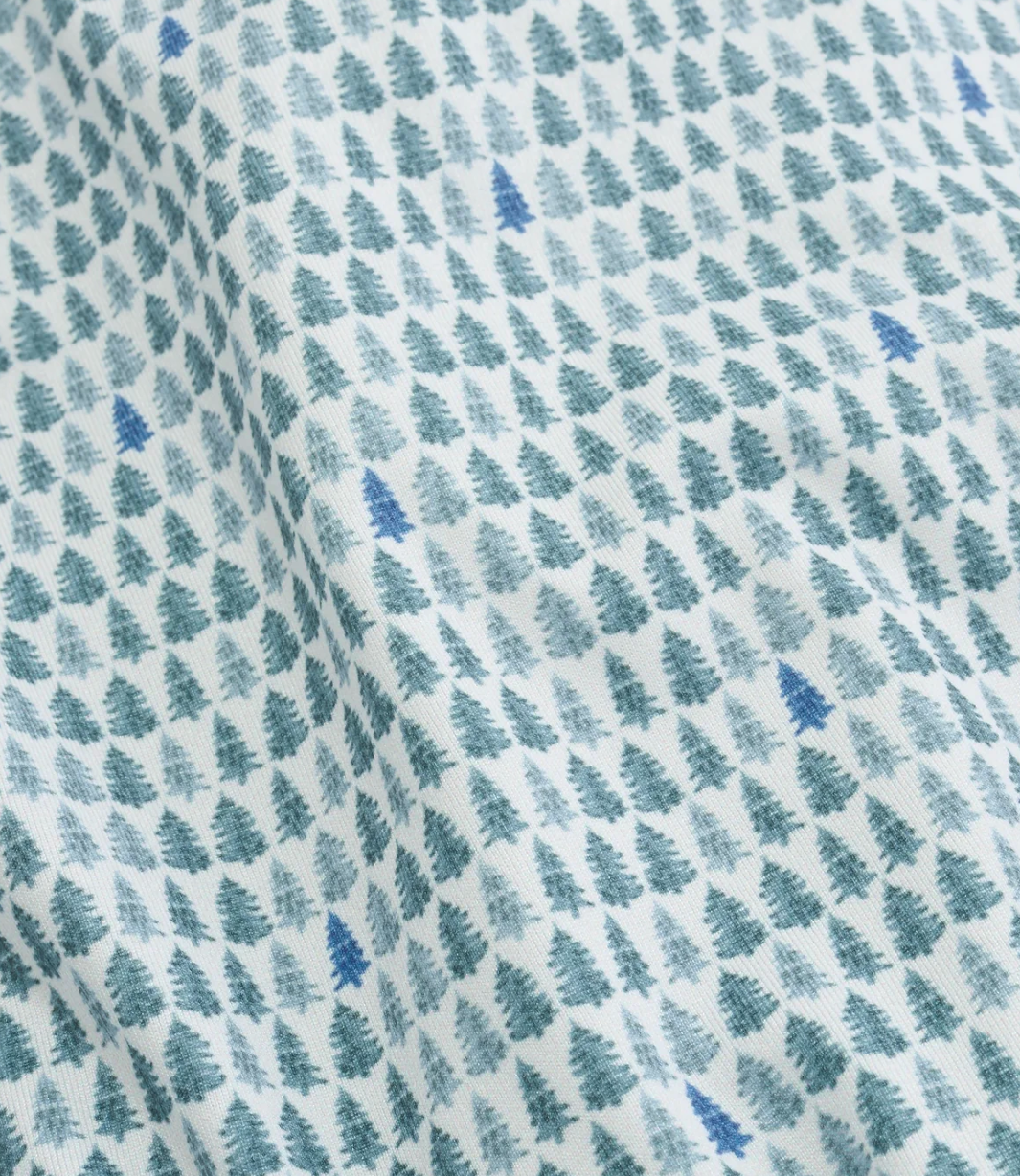 White fabric with a repeating pattern of small Christmas trees in shades of blue and teal, shown with soft folds.