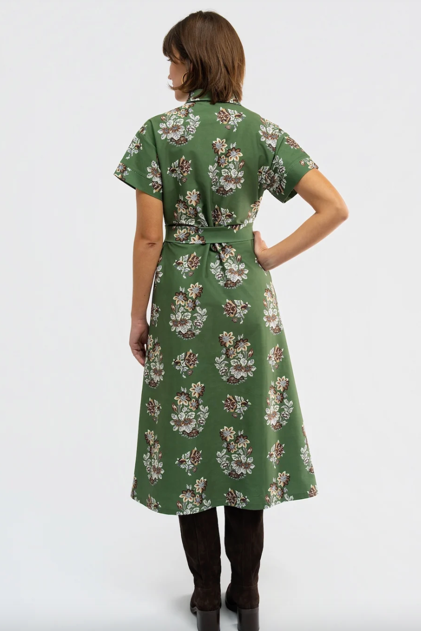 A woman is shown from the back wearing a green short-sleeve midi dress with a white and brown floral pattern, paired with dark brown knee-high boots, against a plain white studio background.