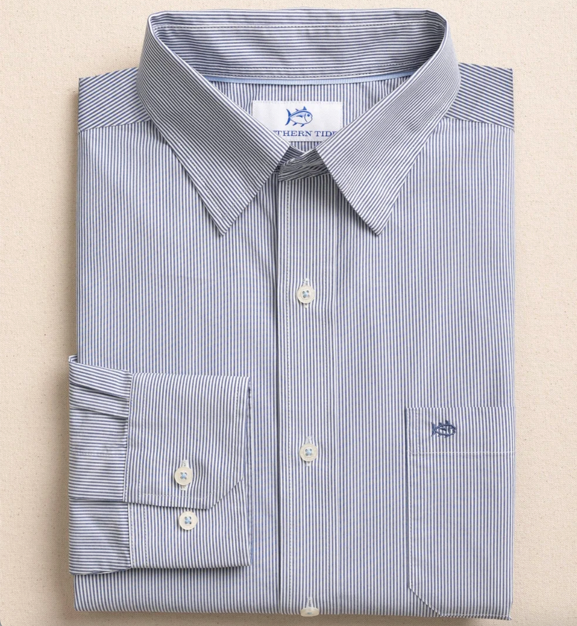 A folded long-sleeve button-down dress shirt with fine vertical blue and white pinstripes, featuring a pointed collar, a single-button cuff, and a chest pocket. The neck label reads Southern Tide.