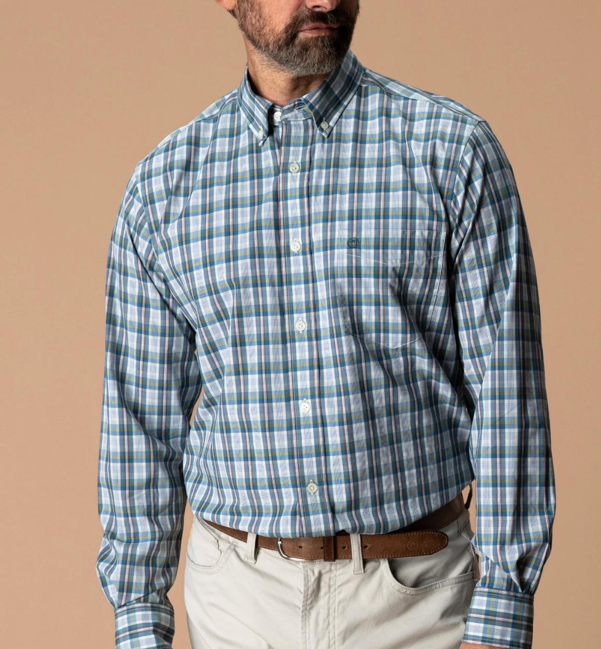A close-up of a man wearing a long-sleeve button-down shirt with a blue, yellow, and red plaid pattern, against a solid beige background.