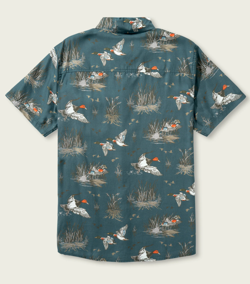 A short-sleeve button-up camp shirt with a teal blue-green background and an allover print of mallards and reeds. The shirt is laid flat against a light beige background.