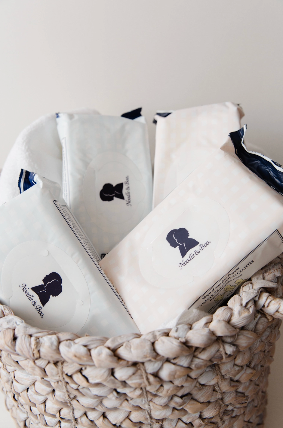 Several white paper packets with dark navy blue branding and text are arranged inside a woven natural-fiber basket against a plain light background.