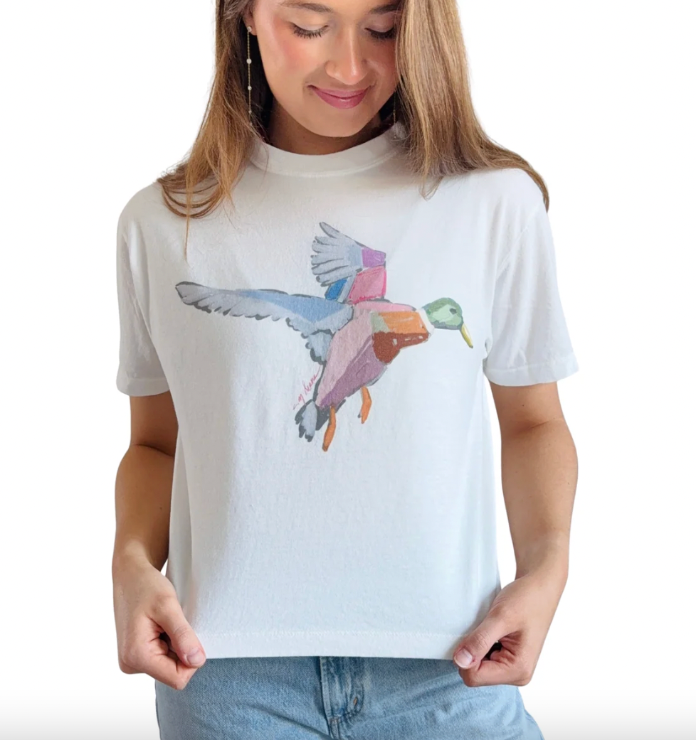 Print of a mallard by Chelsea McShane on a boxy, white, Comfort Colors Tee. Woman is wearing light wash denim bottoms against a white background.