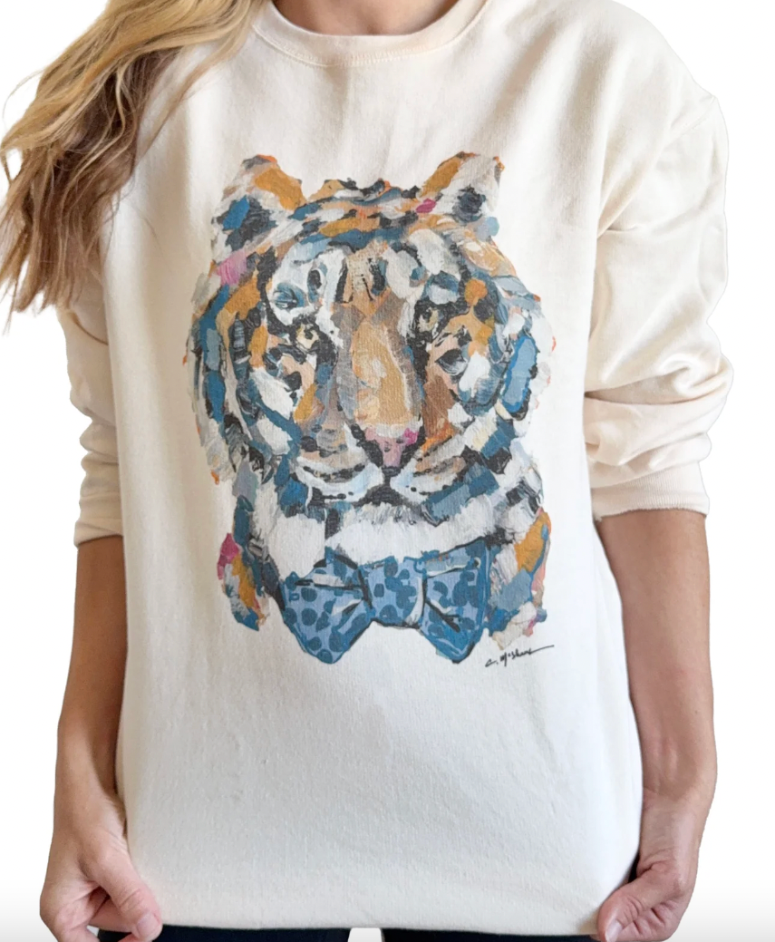 A person wearing a cream-colored crewneck sweatshirt with a large acrylic-style tiger face graphic on the front, featuring blue, orange, and white tones.