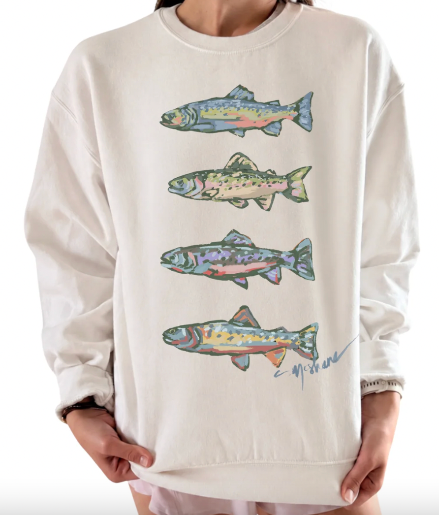 A person wearing a cream sweatshirt with four colorful trout illustrations printed vertically on the front, shown against a plain white background.