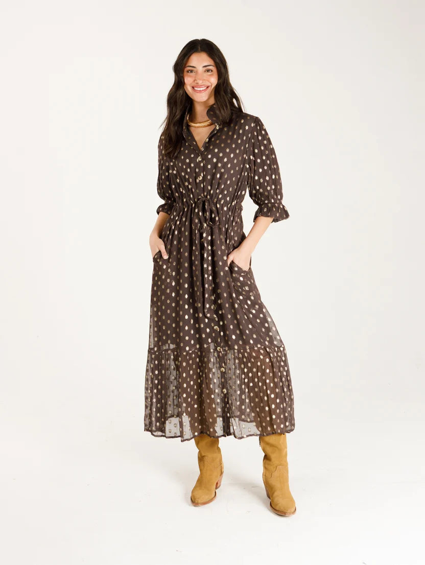 Woman wearing long brown, gold dotted dress that cinches at the waist