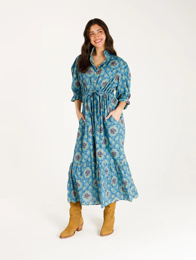 Woman wearing long green dress that cinches at the waist with patterns of blue cane and oak trees